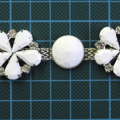 Pulseira branca com flores e strass sobre fundo azul com grade