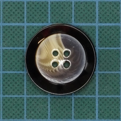 Botão redondo madrepérola com borda preta sobre tecido verde quadriculado