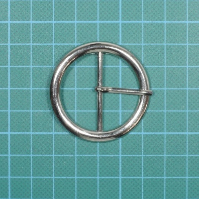 Fivela redonda de metal prateado sobre fundo quadriculado verde