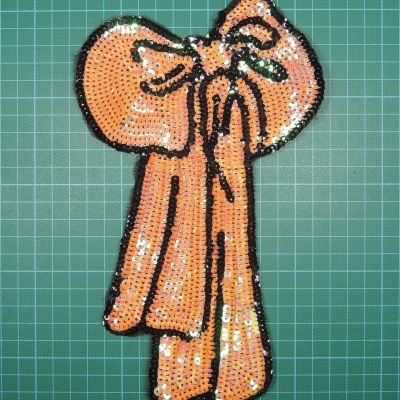 Aplique em forma de laço cor de rosa com lantejoulas sobre fundo quadriculado verde