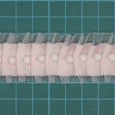 Faixa de tecido rosa com botões e renda cinza sobre base verde com grelha.