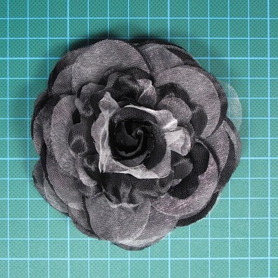 Flor de tecido preta e cinza com pétalas sobrepostas sobre superfície quadriculada verde