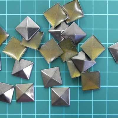 Tachas quadradas metálicas prateadas e douradas sobre fundo verde quadriculado