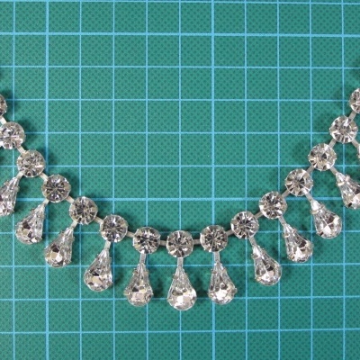 Colar com pedras transparentes facetadas em fundo verde com grade branca.