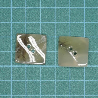 Dois botões quadrados cinza e bege com dois orifícios sobre superfície quadriculada