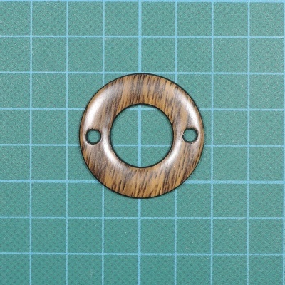 Anel redondo de madeira com dois orifícios sobre superfície quadriculada azul e verde