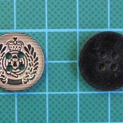 Dois botões, dourado decorativo e preto fosco, sobre fundo verde com grelha.