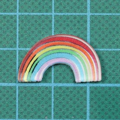 Patch bordado colorido em forma de arco-íris sobre fundo verde quadriculado