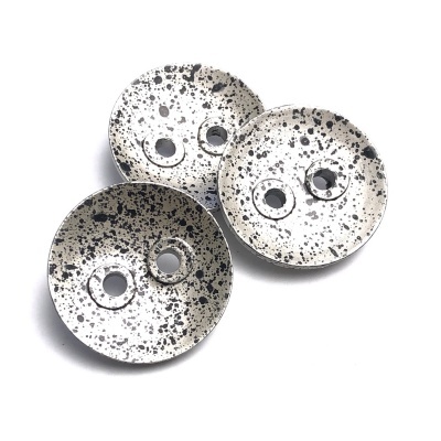 Três pratos de cerâmica brancos com salpicos pretos e dois buracos no centro