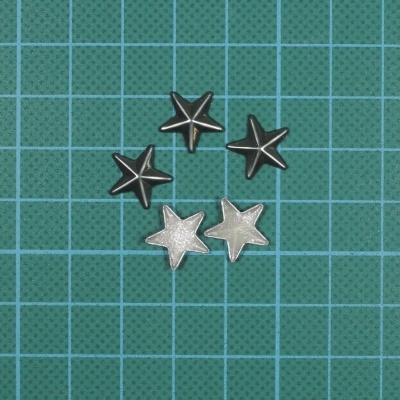 Cinco estrelas metálicas pequenas, três pretas e duas prateadas sobre superfície verde quadriculada