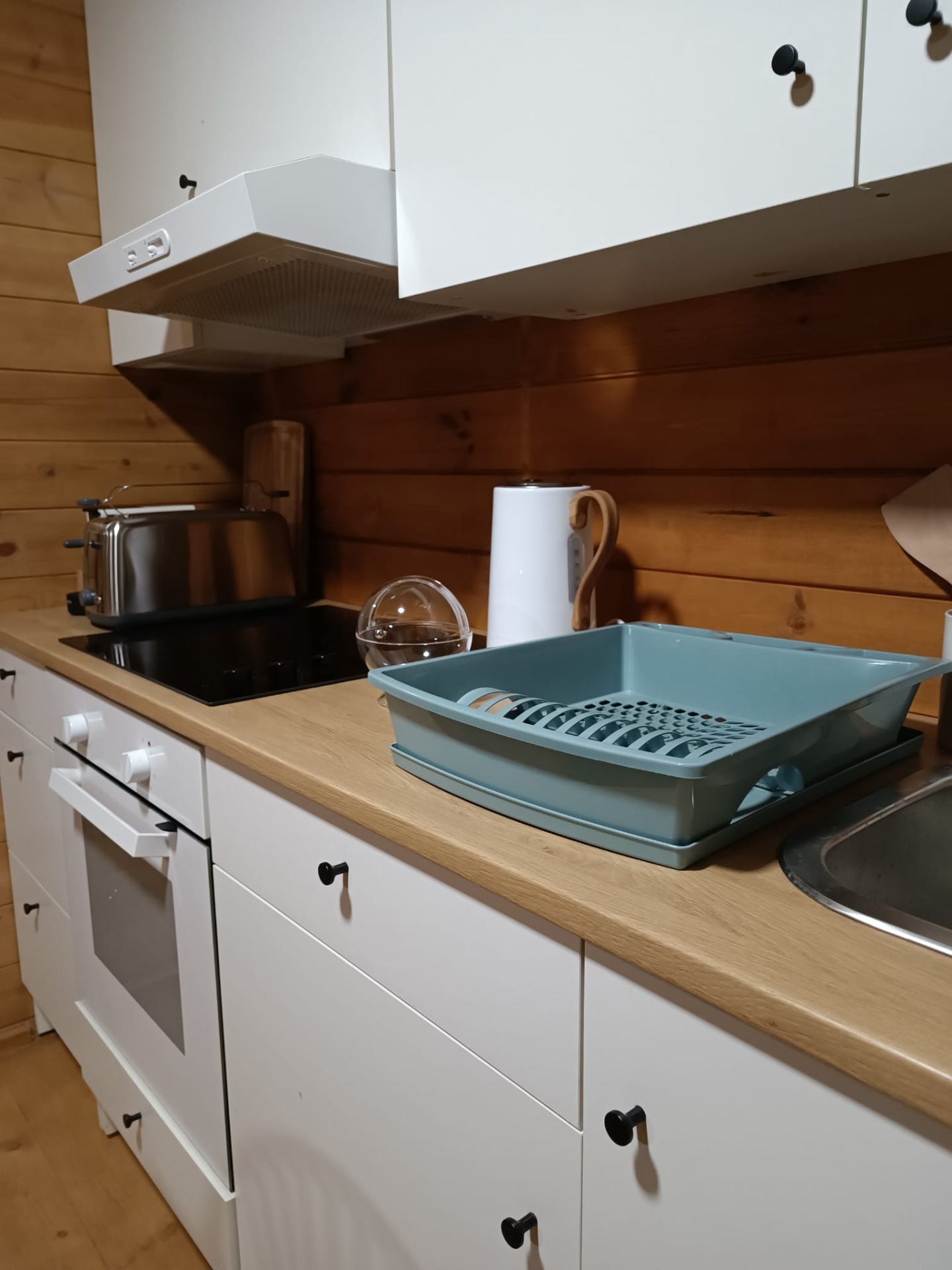 Gift Voucher - Fun Glamping Natura | 2 Noites Cozinha com armários brancos, superfície de madeira clara e utensílios como escorredor de louça azul e torradeira metálica