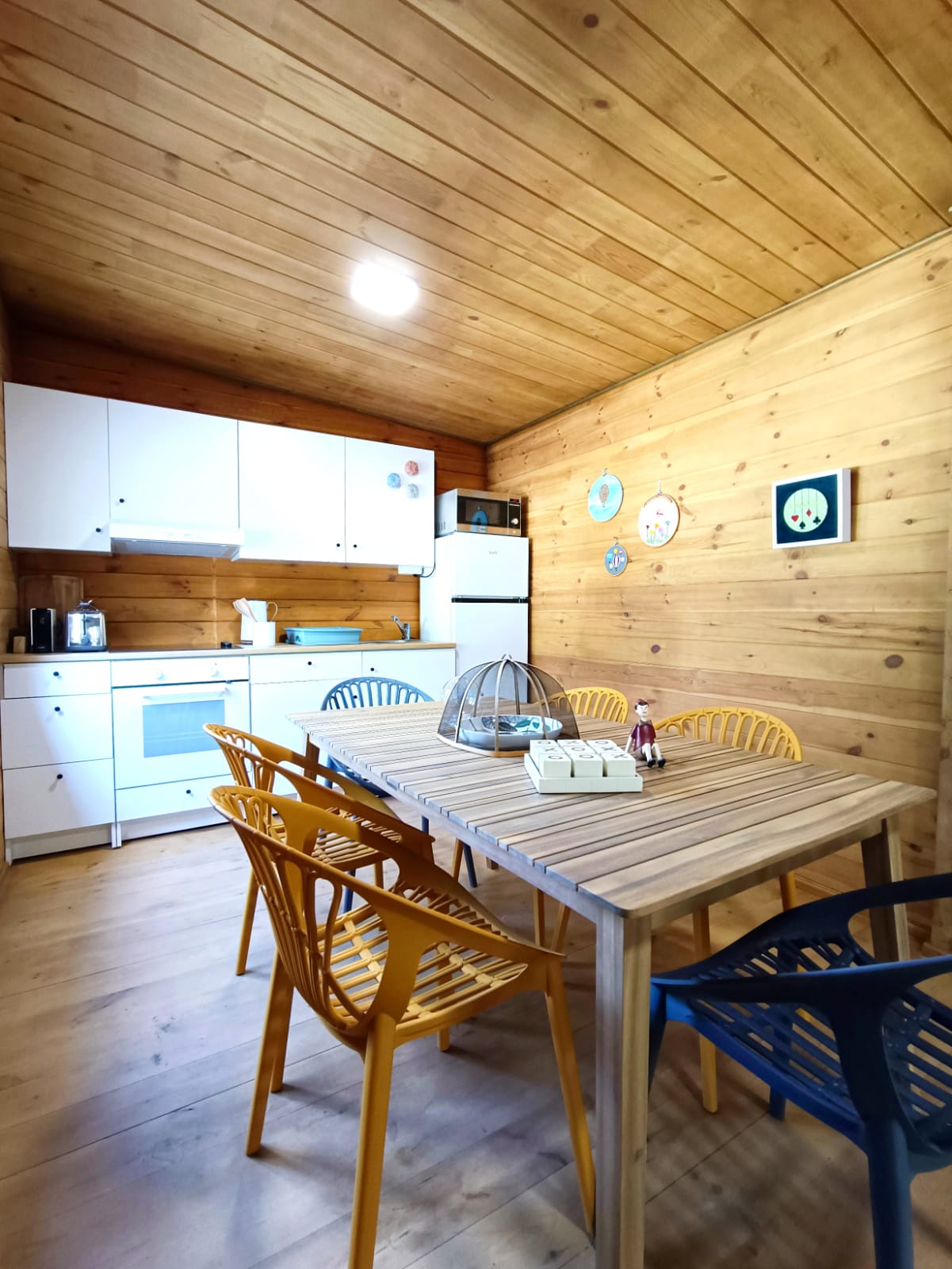 Gift Voucher - Fun Glamping Natura | 2 Noites Cozinha de madeira com móveis brancos e cadeiras amarelas e azuis