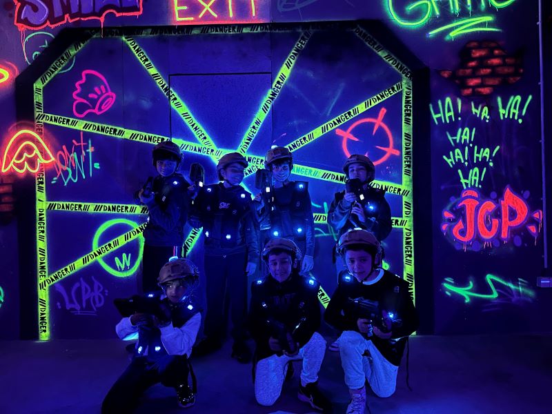 Gift Voucher - Xtreme Laser Tag, Sintra | 5 pessoas Crianças com coletes LED azuis e capacetes posando diante de parede com fitas reflexivas e grafites coloridos