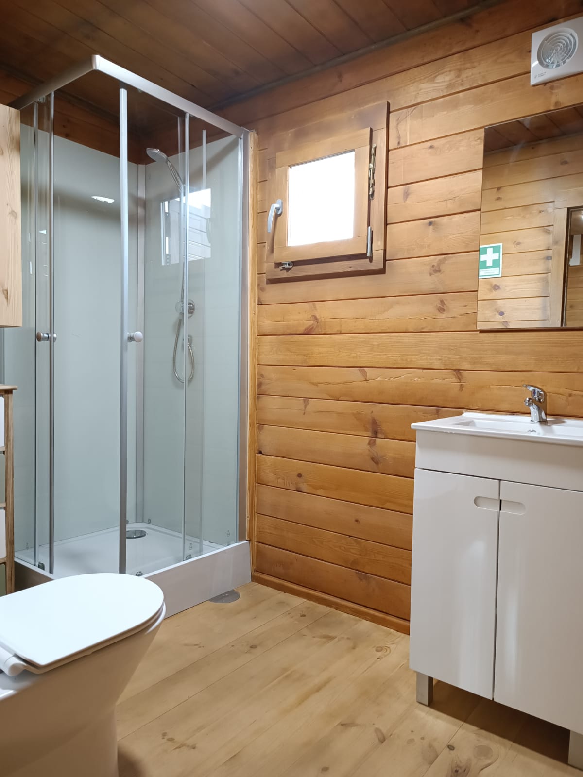 Gift Voucher - Fun Glamping Natura | 2 Noites Casa de banho com madeira clara, cabine de duche em vidro, sanita e móvel de lavatório branco.