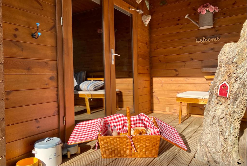 Gift Voucher - Fun Glamping Natura | 2 Noites Varanda em madeira com cesto de piquenique e porta de vidro aberta