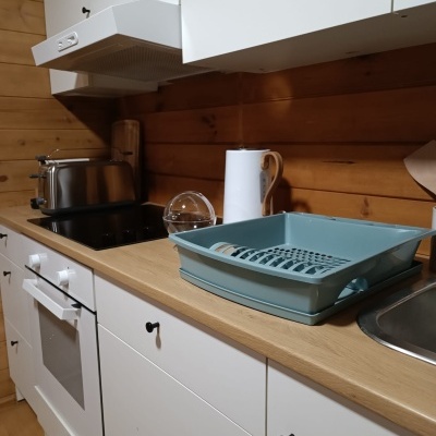 Cozinha com armários brancos, superfície de madeira clara e utensílios como escorredor de louça azul e torradeira metálica