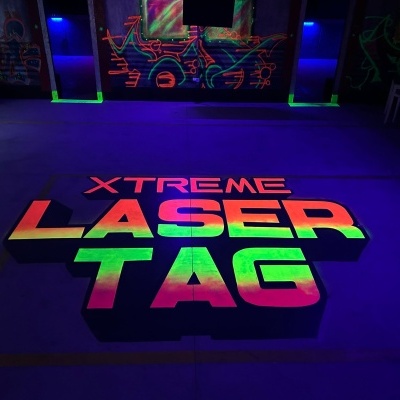 Piso escuro com texto colorido 'XTREME LASER TAG' e grafites neon ao fundo.