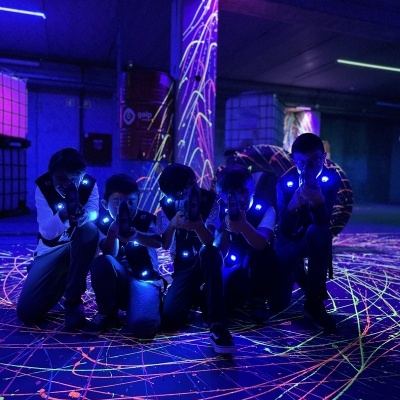 Cinco pessoas com coletes e armas de laser num espaço com iluminação neon