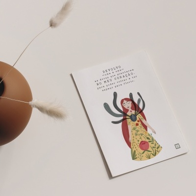 Vaso de cerâmica castanho com ramos secos e cartão ilustrado com texto em português