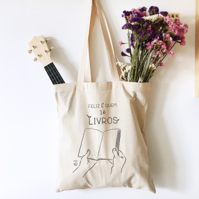 Saco de tecido bege com texto e desenho pendurado na parede com flores e instrumento musical