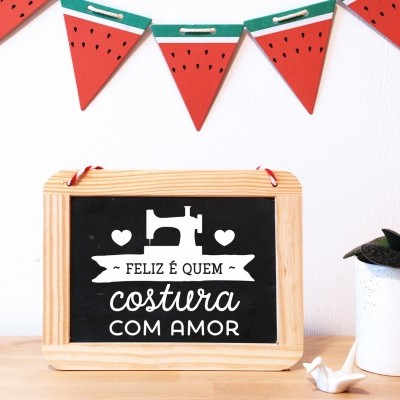 Painel decorativo de madeira com mensagem sobre costura, vaso com suculenta e guirlanda de melancia