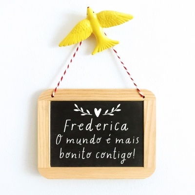 Quadro decorativo com texto em português pendurado por cordão e com ave amarela