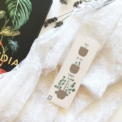 Marcador de livro com desenhos de vasos de plantas junto a tecido branco e livro preto