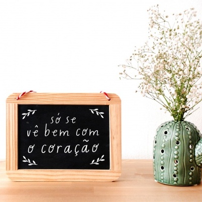 Quadro com frase em português e vaso em forma de cacto com flores brancas