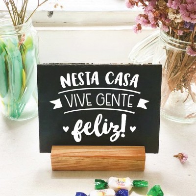 Placa preta com texto branco numa base de madeira entre frascos de vidro com flores e pedras coloridas