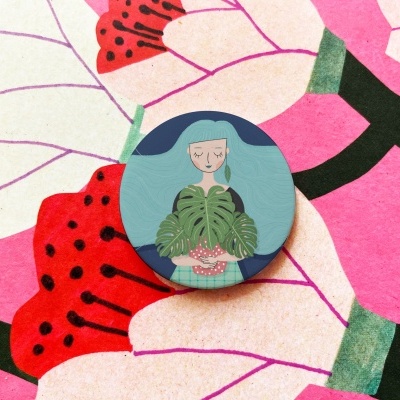 Botão decorativo redondo com ilustração de mulher segurando planta sobre tecido floral colorido