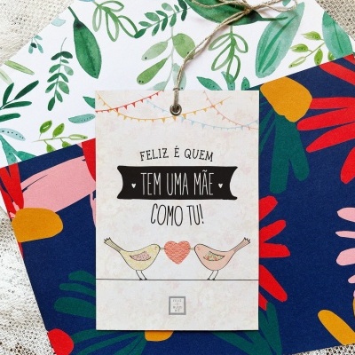 Cartão com mensagem para mãe pendurado sobre dois envelopes coloridos florais