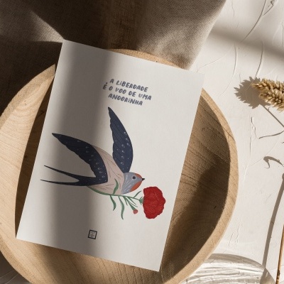 Cartão ilustrado com uma andorinha azul e bege segurando uma flor vermelha num prato de madeira natural.