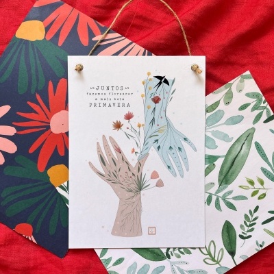 Folhas de papel decorativo com padrões florais e texto em português, sobre tecido vermelho.