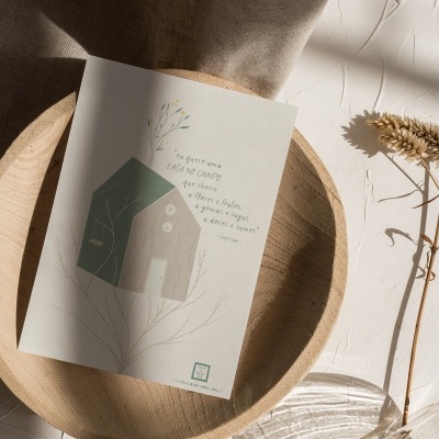 Cartão postal com ilustração de casa e texto numa travessa de madeira, ramo seco ao lado