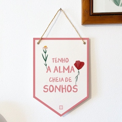 Placa decorativa branca com texto e flores pendurada na parede