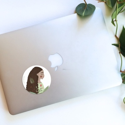 Portátil Apple cinzento prateado com autocolante de mulher e plantas verdes ao lado