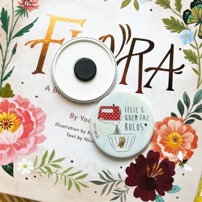 Dois bottons redondos sobre livro com capa floral e texto 'FLORA'