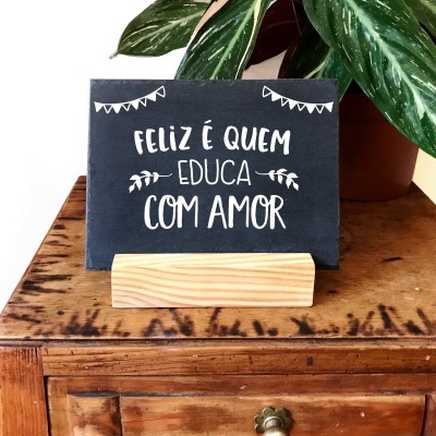 Cartaz cinza escuro com texto branco sobre suporte de madeira em móvel com planta ao lado