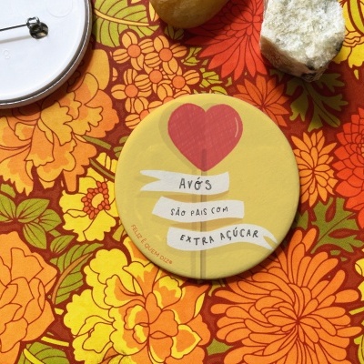 Botão amarelo redondo com coração vermelho e texto sobre tecido floral colorido