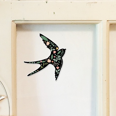 Adesivo de andorinha com padrão floral numa porta branca com moldura e móbile de gaivota pendurado