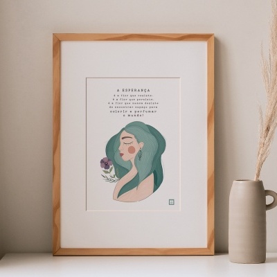 Quadro ilustrado com moldura de madeira e texto em português, colocado numa superfície branca ao lado de vaso cinzento com flor seca