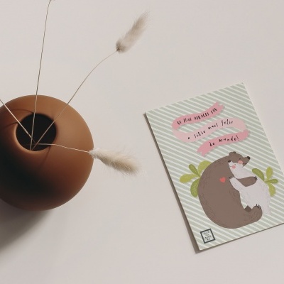 Vaso de cerâmica castanha com ramos secos e postal com desenho de esquilo e texto motivacional