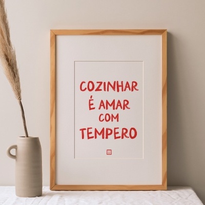 Quadro com texto vermelho numa moldura de madeira, vaso cinzento com planta seca ao lado