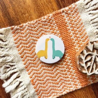 Botão redondo colorido sobre tecido laranja e creme com franjas e carimbo de madeira ao lado