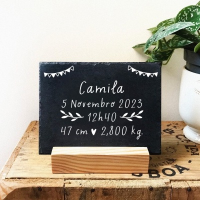 Placa preta com texto branco sobre base de madeira ao lado de vaso com planta