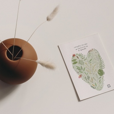 Vaso cerâmico marrom com ramos secos e cartão com ilustração de coração verde e texto em português