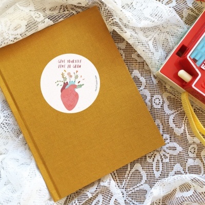 Livro amarelo mostarda com etiqueta e máquina fotográfica vermelha Fisher-Price sobre renda branca