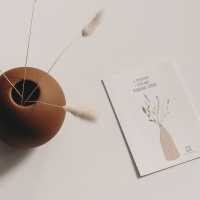 Vaso de cerâmica castanha com hastes secas e cartão ilustrado ao lado