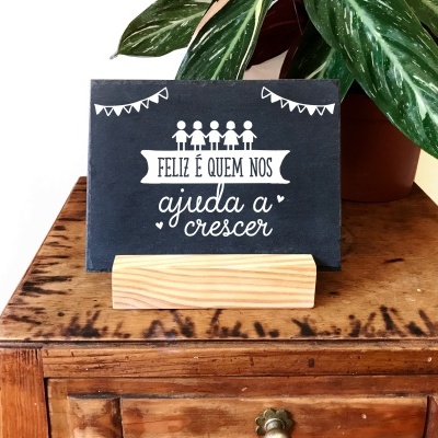 Cartão com frase decorativa em suporte de madeira sobre móvel antigo com planta ao fundo