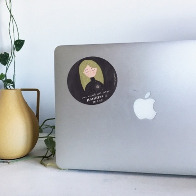 Computador Apple prateado com autocolante e vaso amarelo com planta verde.